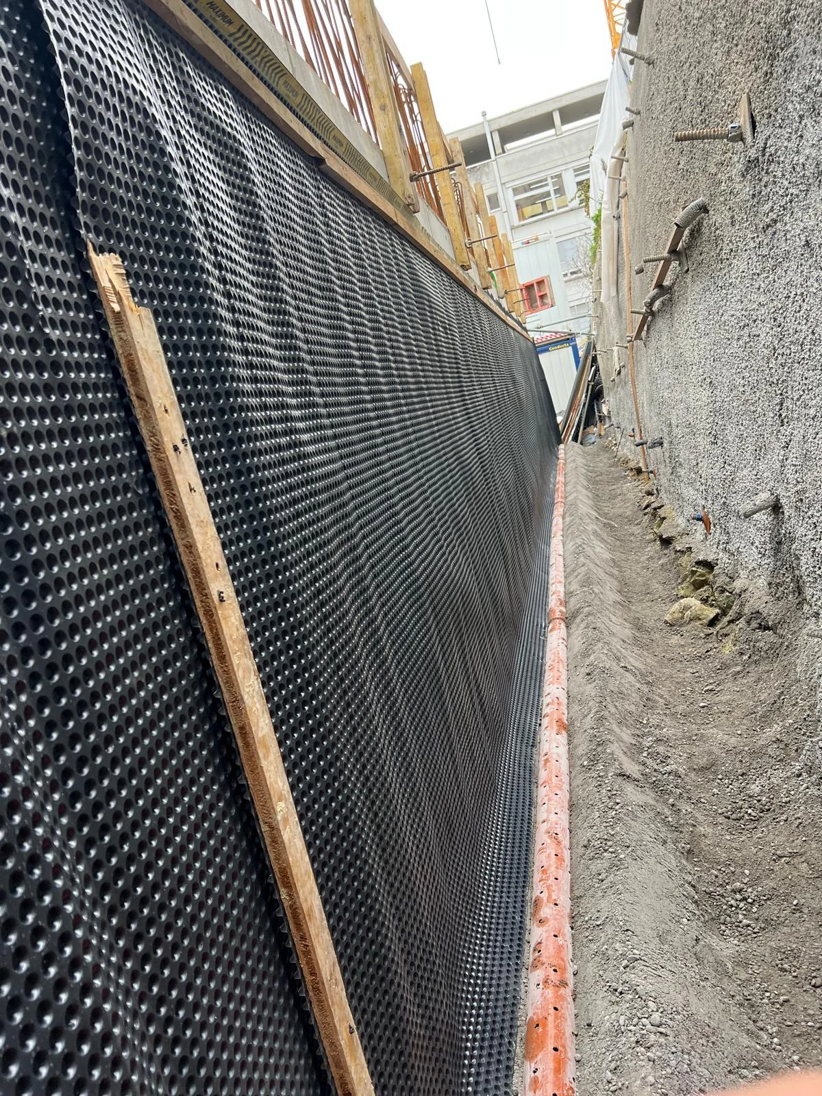 Nappe à excroissances contre un mur et drain orange au fond de la fouille